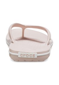 Des tongs en caoutchouc rose clair avec une semelle texturée, des lanières fines et un bandeau blanc arborant le logo "CROCS" au talon.