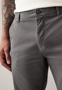 Gray cotton trousers featuring a smooth texture, slim fit, button closure, and detailed stitching on pockets. Hand resting on thigh.