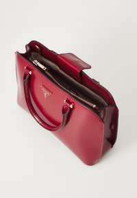 Borsa a mano rossa lucida con manici doppi, chiusura con zip e scomparto interno. Presenta una placca con logo e una texture liscia.