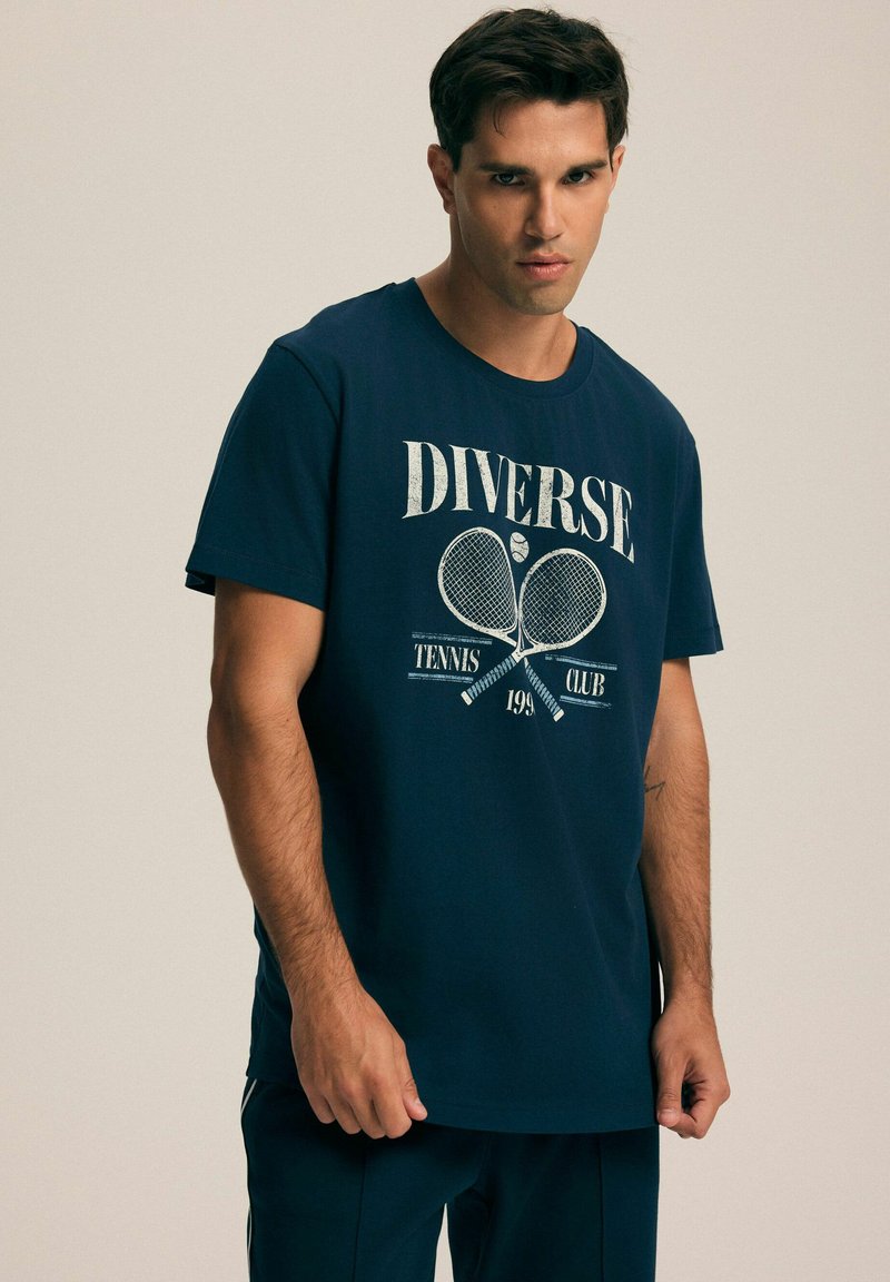 Granatowa bawełniana koszulka z białym napisem graficznym "Diverse" oraz tenisowym motywem, z rakietami i piłką. Klasyczny krój z okrągłym dekoltem.