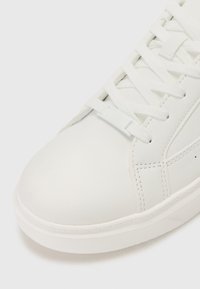 White sneakers with a smooth leather texture, rounded toe, and flat lace-up design. Subtle stitching details and minimalistic side accents.