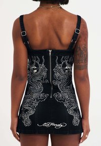 Zwarte denim jurk met verstelbare bandjes, met witte draak borduursels, een rits aan de achterkant en het "Ed Hardy"-logo aan de zoom.