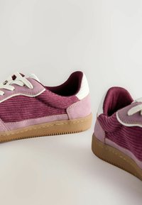 Lila kordflamsneakers med rosa mockadetaljer och vita läderdetaljer. Har runda snören och en texturerad gummisula.