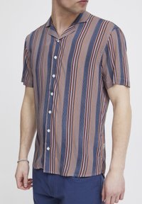 Camicia a maniche corte con colletto a profilo, caratterizzata da strisce verticali blu, rosse e crema, realizzata in tessuto leggero con chiusura a bottoni.