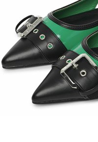 Zapatos negros y verdes con punta afilada y un acabado brillante, que presentan una hebilla decorativa y acentos metálicos, cuero texturizado y detalles de ojales.