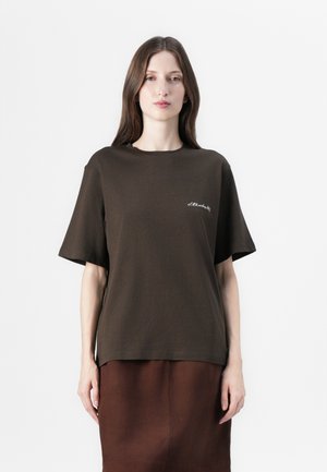 Brown cotton t-shirt with short sleeves, relaxed fit, and a small white embroidered detail on the left chest. Worn with a matching brown skirt.