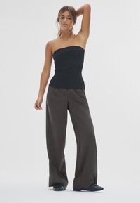 Zwart topje zonder bandjes, getailleerd bij de taille, gecombineerd met hooggetailleerde, wijdvallende donkerbruine broek. Gladde texturen, minimale details.