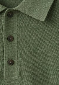 Close-up van een olijfgroen gebreid poloshirt met drie donkere knopen en een gestructureerde kraag.