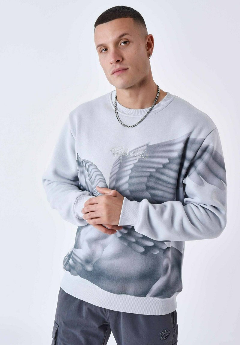 Grijze sweatshirt met gedetailleerde vleugelafbeelding, geribde manchetten en tailleband. Model draagt een zilveren ketting. Achtergrond is effen wit.