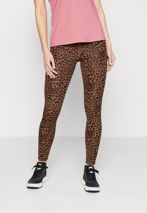 Leggings de estampado de leopardo en marrón con manchas negras, diseño ajustado y tejido elástico, combinados con zapatillas deportivas negras y una camiseta rosa.