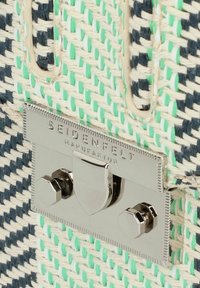 Bolsa tejida que presenta una mezcla de hilos en azul marino y verde menta, un cierre de metal plateado elegante con marca y una superficie texturizada.