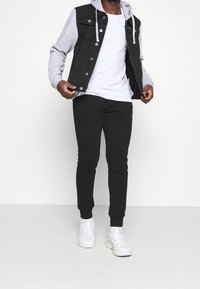 Czarna jeansowa kamizelka z szarymi rękawami od bluzy z kapturem, biała koszulka oraz czarne spodnie dresowe. Całość dopełniają białe trampki.