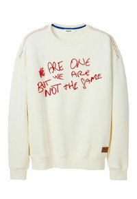Sudadera color crema con texto bordado en rojo: "SOMOS UNO PERO NO SOMOS IGUALES." Presenta puños acanalados y una etiqueta en el dobladillo.