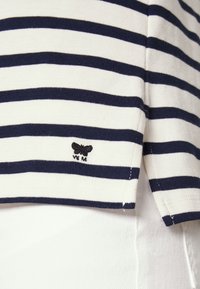 Gestreiftes T-Shirt aus Creme und marineblauem Baumwollstoff, mit einem kleinen schwarzen Schmetterlingslogo am Saum und einer figurbetonten Passform.