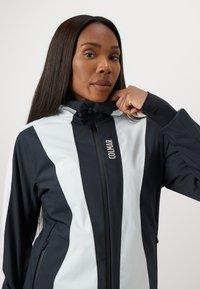Schwarz-weiße Sportjacke mit hohem Kragen, Reißverschluss vorne und dezentem Branding. Verfügt über kontrastierende Farbblöcke und eine taillierte Passform.