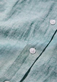 Gros plan sur un tissu vert clair avec une couture et deux boutons ronds blancs cousus.