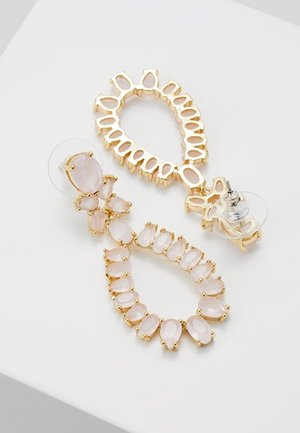 Kolczyki na sztyft w kolorze złotym z przezroczystymi i różowymi kamieniami w kształcie kropli, ułożonymi w otwarte owalne i klastrowe wzory, z przezroczystymi zapięciami.