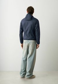Marineblaue leichte Jacke mit Kapuze, ausgestattet mit einer glatten Textur und elastischen Bündchen, kombiniert mit hellblauen, locker sitzenden Jeans.