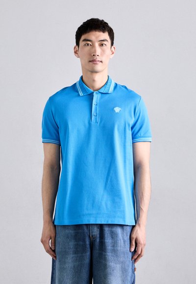 Lichtblauwe polo met een gestructureerde kraag en een drie-knopen sluiting. Beschikt over contrasterende gestreepte accenten op de kraag en mouwen.
