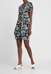 Kwiatowa sukienka z krótkim rękawem w granatowym kolorze z różowymi i zielonymi nadrukami roślinnymi. Posiada ściągnięty w pasie krój, okrągły dekolt oraz lekką tkaninę.