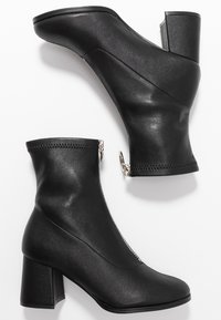 Bottes noires en simili cuir, avec un talon carré, des zips sur les côtés et une conception épurée.