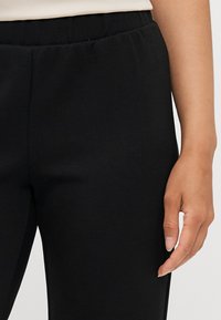 Sorte skreddersydde bukser med en glatt tekstur, elastisk midjebånd og sidelommer. Kuttingen er rett, noe som fremhever et raffinert, klassisk design.