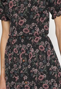 Vestido preto floral com mangas curtas em balão. Apresenta flores rosas e azuis em tecido texturizado, complementado por botões de madeira castanha.