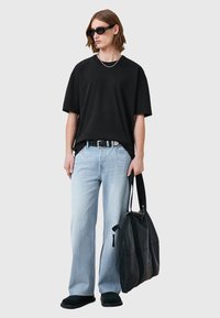 T-shirt nera oversize, jeans in denim azzurro chiaro, cintura nera, occhiali da sole neri e una grande borsa tote nera con zip. Scarpe nere in suede.