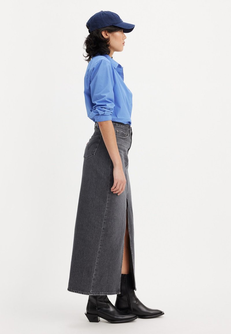 Camisa azul de manga larga, falda maxi de denim gris con abertura lateral y botas negras de tobillo con tacón geométrico, todo sobre un fondo blanco.