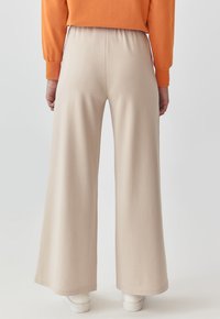 Pantaloni bej cu croi larg, cu un talie elastică, textură netedă și detalii de cusătură subtile, asortați cu adidași albi.