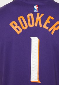Lilla basketballtrøje med "BOOKER" i orange bogstaver og nummer "1" i hvid med orange kant. NBA-logo øverst til højre.