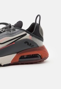 Grå sportskor med en strukturerad yta, röda accenter, svart sula och synlig luftkuddar. Består av mesh och syntetiska material.