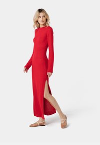 Red long-sleeve dress with a fitted silhouette and a side slit, crafted from a textured, soft fabric. Paired with light brown woven flats.