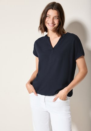 Blusa navy a maniche corte con scollatura a V e vestibilità rilassata; realizzata in tessuto leggero. Abbinata a pantaloni bianchi.