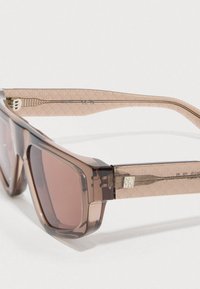 Óculos de sol transparentes castanhos com padrão geométrico nas hastes marmoreadas. Possuem lentes retangulares e detalhes metálicos na dobradiça.