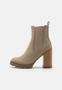 Botte de cheville en daim taupe avec un talon épais empilé, des panneaux élastiques sur les côtés, une anse de traction et une semelle en caoutchouc crantée.