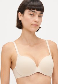 Beige bh med glatt stoff, underwire støtte og dyp utringning. Justerbare stropper og sømløse kopper for et strømlinjeformet utseende.