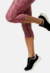 Tight siddende lyserøde leopardmønstret capri leggings med en glat tekstur, parret med sorte træningssko med en hvid sål og lyserøde accenter.