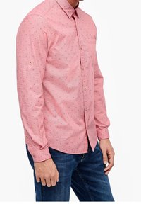 Camicia rosa chiaro con piccoli punti blu, colletto a bottoni, maniche lunghe e taschino sul petto. Realizzata in un tessuto con una sottile texture.