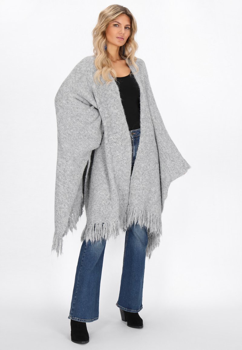 Harmaa ylisuuri poncho, joka on valmistettu teksturoidusta kankaasta ja jonka helmassa on fringed yksityiskohtia. Yhdistetty leveälahkeisiin farkkuihin ja mustiin nilkkabootseihin.
