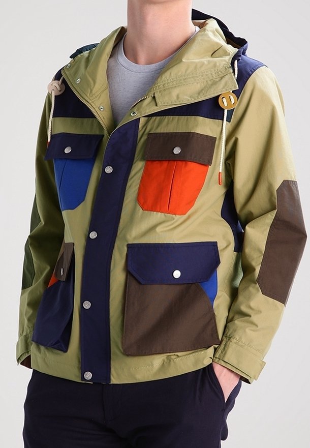 Kolorowa kurtka z wieloma kieszeniami, wykonana z lekkiego materiału. Posiada mieszankę odcieni oliwkowej zieleni, niebieskiego, pomarańczowego i brązowego oraz kaptur.