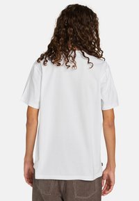 T-shirt bianco a maniche corte con vestibilità rilassata, colletto a giro e tessuto di cotone morbido. Cuciture a vista e logo del marchio sull'orlo.
