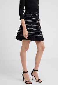Schwarzer Rock mit weißen horizontalen Streifen, mit einem ausgestellten Design und einem strukturierten Strickmaterial. Getragen mit schwarzen, Riemchen-High Heels.
