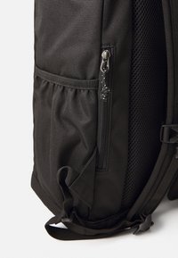 Zaino nero realizzato in tessuto resistente, dotato di una tasca laterale con chiusura a zip, inserti in rete e spallacci regolabili per una maggiore comodità di trasporto.