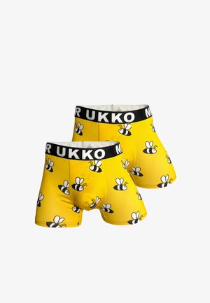 Dwie żółte bokserki z czarnymi pasami w talii z napisem "MUKKO", ozdobione powtarzającym się wzorem czarno-białych kreskówkowych pszczół.