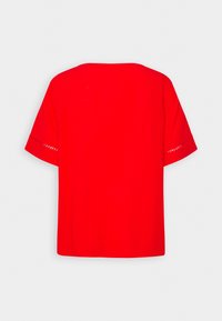 Haut rouge à manches courtes avec une coupe ample, un col arrondi et des détails décoratifs ajourés le long des manches. Texture lisse sur toute la surface.