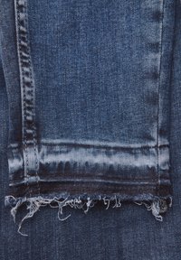 Niebieskie dżinsy z postrzępionym dołem. Materiał jest wytrzymały o średniej wadze, z lekkim blaknięciem i widocznymi detalami przeszycia wzdłuż boków.