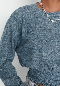 Niebieski, teksturowany krótki sweter o luźnym kroju, z marszczonym, elastycznym dołem i okrągłym dekoltem. Projekt podkreśla srebrny łańcuszek.