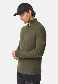 Dark green ribbed pullover sweater with a half-zip collar, featuring a leather accent on the left sleeve and textured detailing on the shoulders.