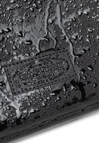 Material negro impermeable con una superficie texturizada, que presenta gotas de agua y un logotipo en relieve en el centro.